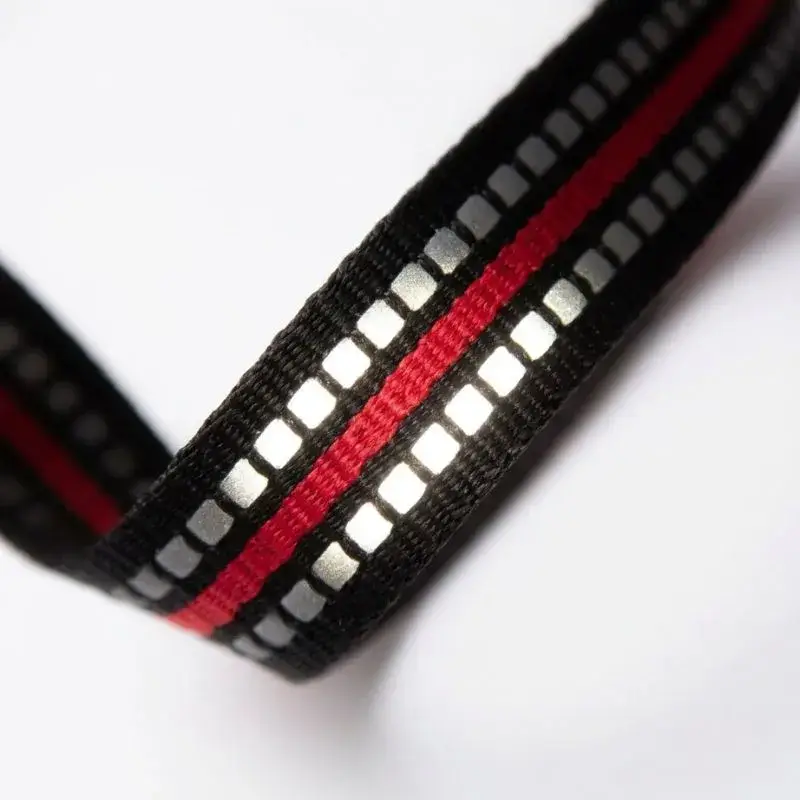 Gros plan sur la sangle en nylon noir et rouge du harnais pour chien Country Plus, illuminée par ses doubles coutures réfléchissantes 3M.